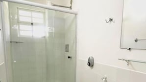 Un baño con ducha de mampara de vidrio, inodoro, lavamanos y espejo.