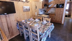 A cozy wooden cabin with a dining area, kitchen, and a TV mounted on the wall. - Cozy chalet in Les Gets center, 4-5 ppl, balcony, garage (Les Gets)