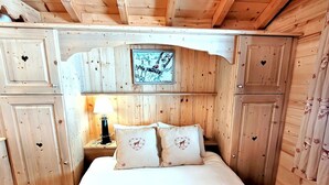 A wooden cabin room with a bed, a nightstand with a lamp, and a framed picture on the wall. - Cozy chalet in Les Gets center, 4-5 ppl, balcony, garage (Les Gets)