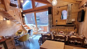 A cozy cabin interior with a wooden staircase, a dining area with a patterned tablecloth, and a television mounted on the wall. - Cozy chalet in Les Gets center, 4-5 ppl, balcony, garage (Les Gets)