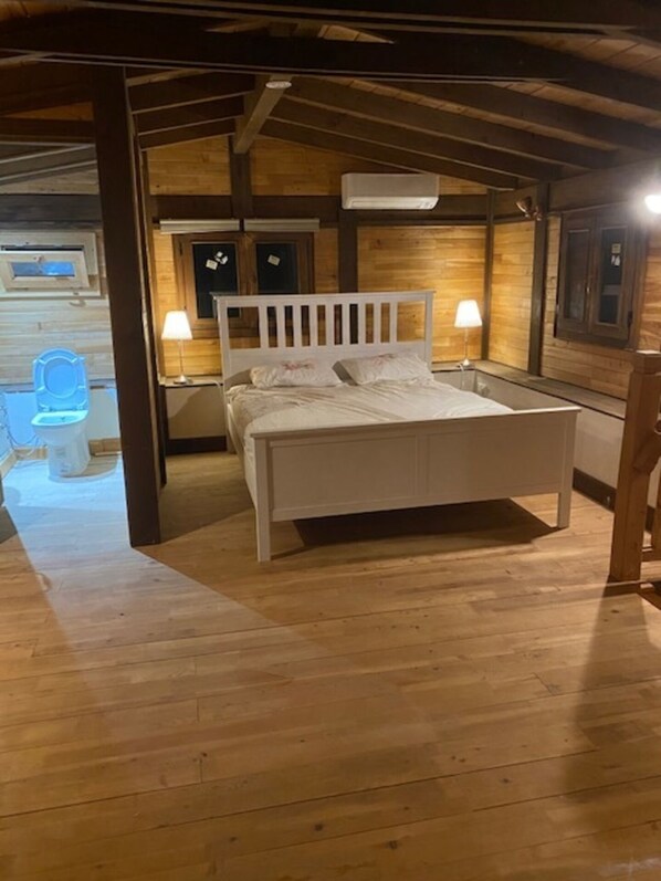 A wooden-floored bedroom with a white bed, two bedside lamps, and a wooden headboard.