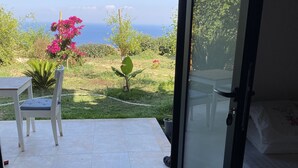 Et værelse med en skydedør til en terrasse med et bord og en stol, en seng og havudsigt.