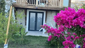 Et træhus med balkon, stenvæg og en have med lyserøde blomster.