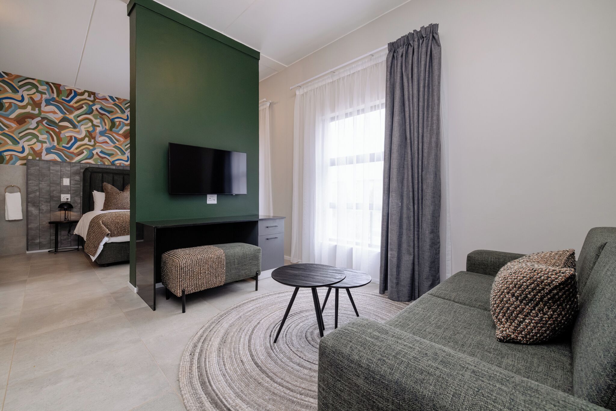 A modern living room with a green accent wall, a flat-screen TV, a round coffee table, and a sofa with a textured throw pillow.