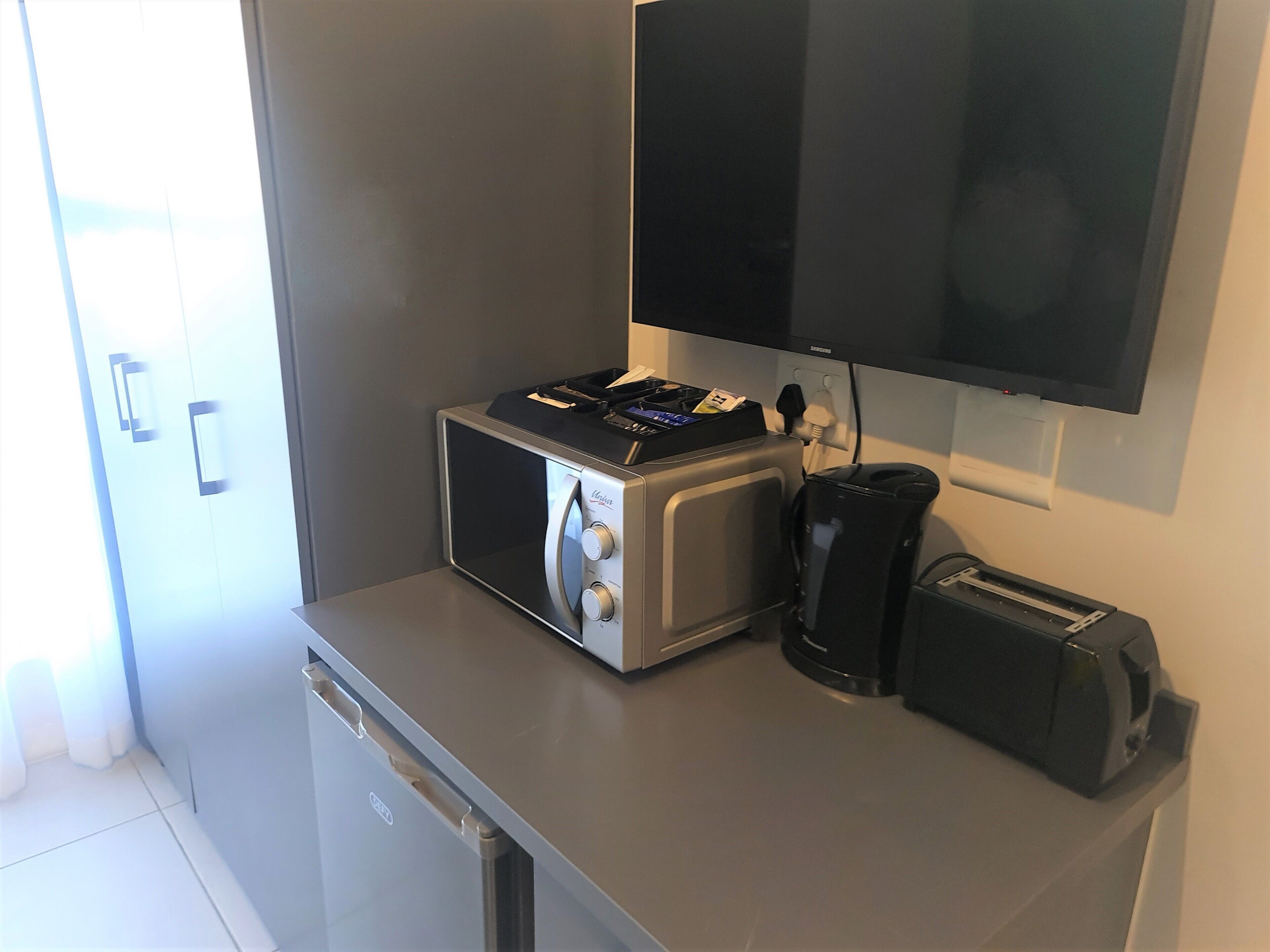 A kitchenette with a microwave, toaster, coffee maker, and a small refrigerator.