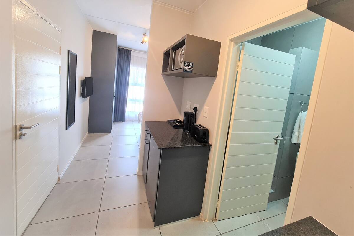 A narrow hallway with a kitchen area on the right, featuring a microwave, toaster, and sink.