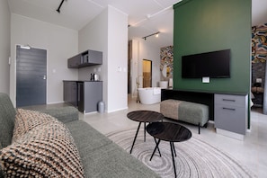 A modern living room with a sofa, a coffee table, a TV, and a green accent wall. - MINT Express Melrose View (Johannesburg)