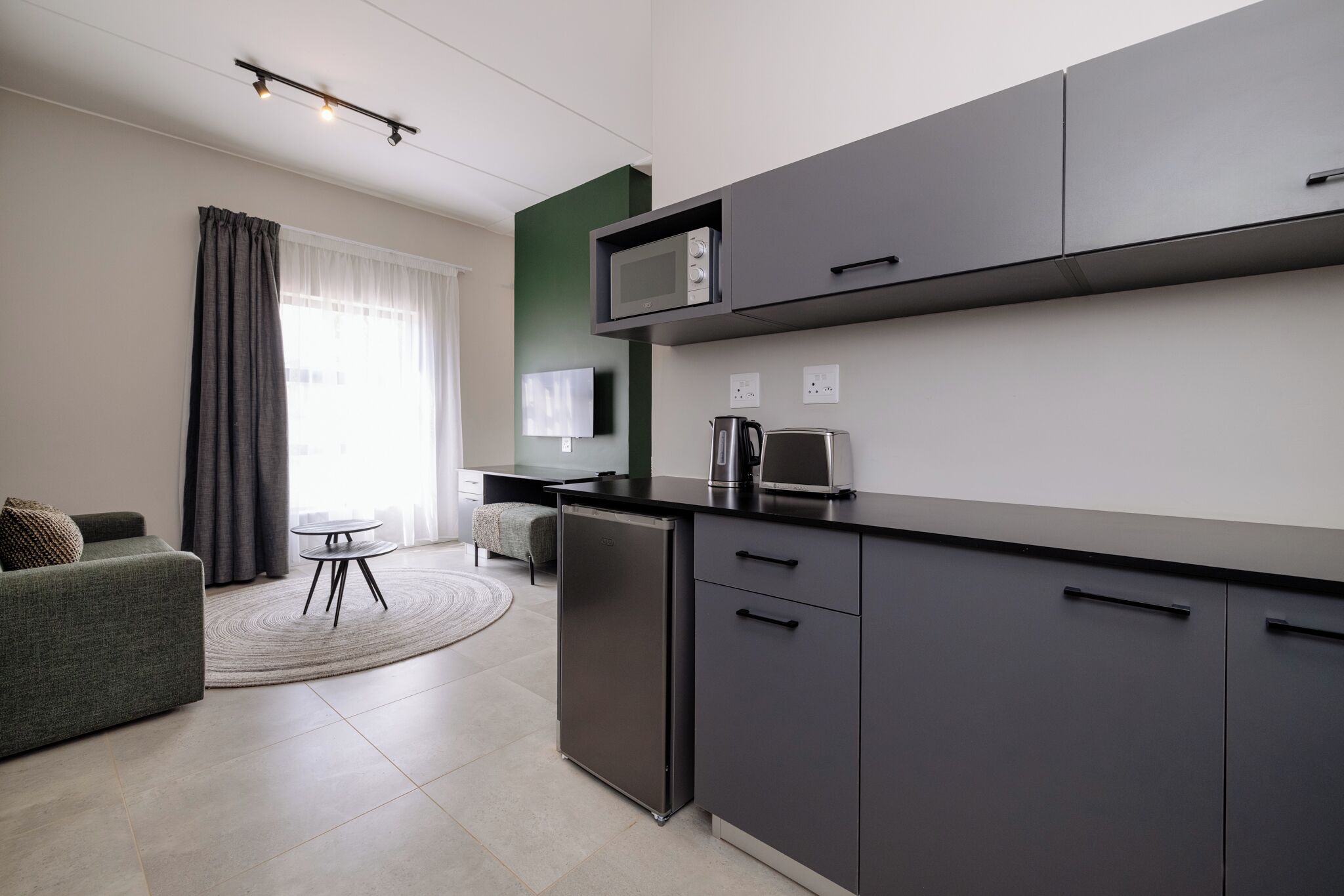 Una cocina moderna equipada con microondas, cafetera y refrigerador. Hay un comedor con una mesa redonda y un sofá.