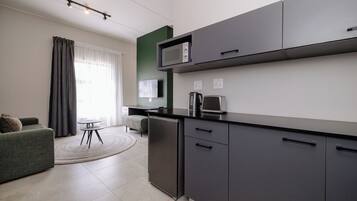 Eine moderne Küche mit integriertem Mikrowellenherd, einer Kaffeemaschine und einem Kühlschrank. Es gibt einen Essbereich mit einem runden Tisch und einer Couch.