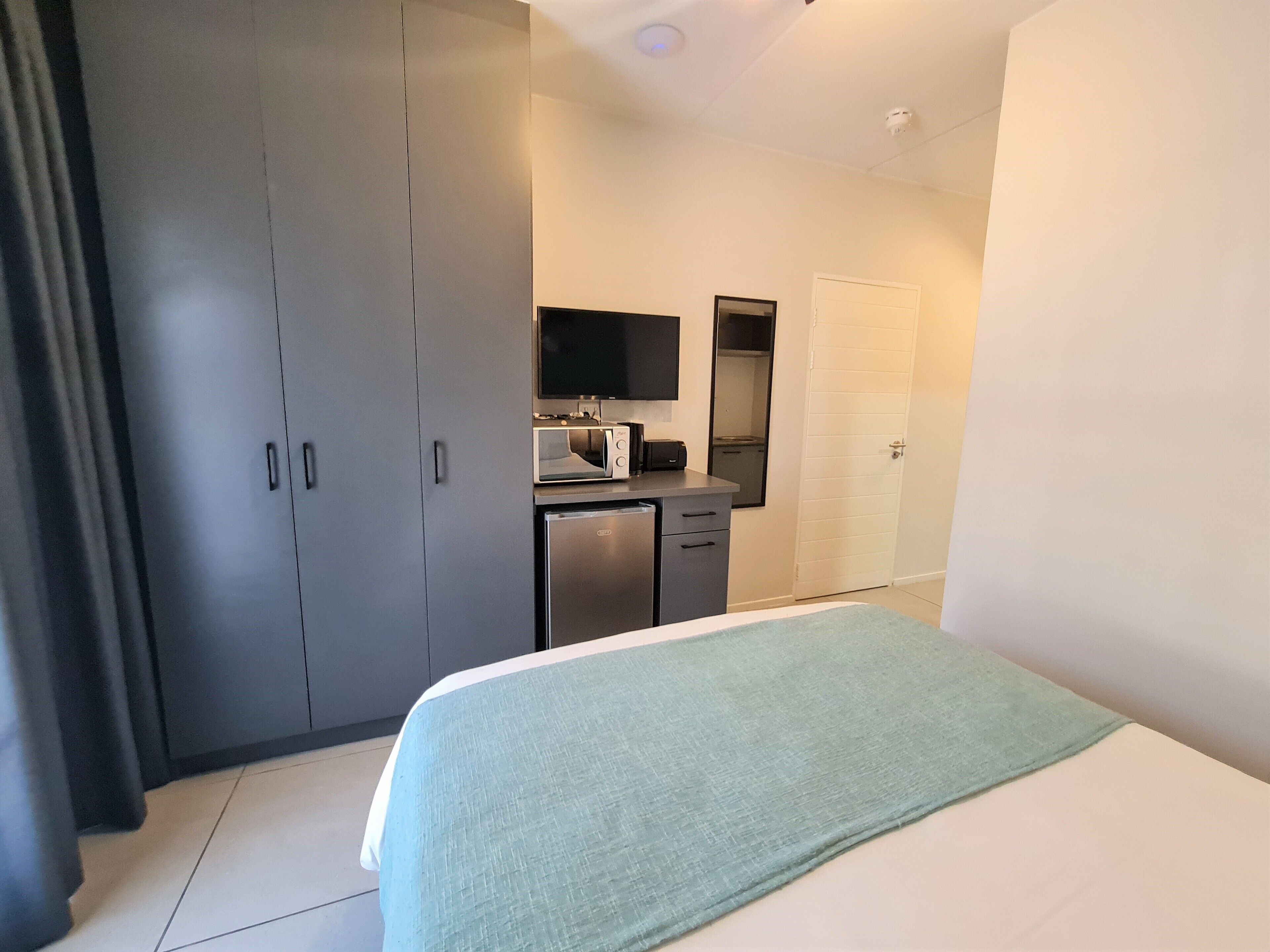 A hotel room with a bed, a wardrobe, a small kitchenette with a microwave, and a television.