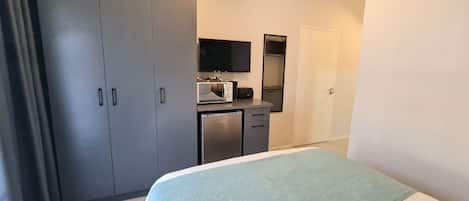 Habitación de hotel con cama, armario, una pequeña kitchenette con microondas y televisión.