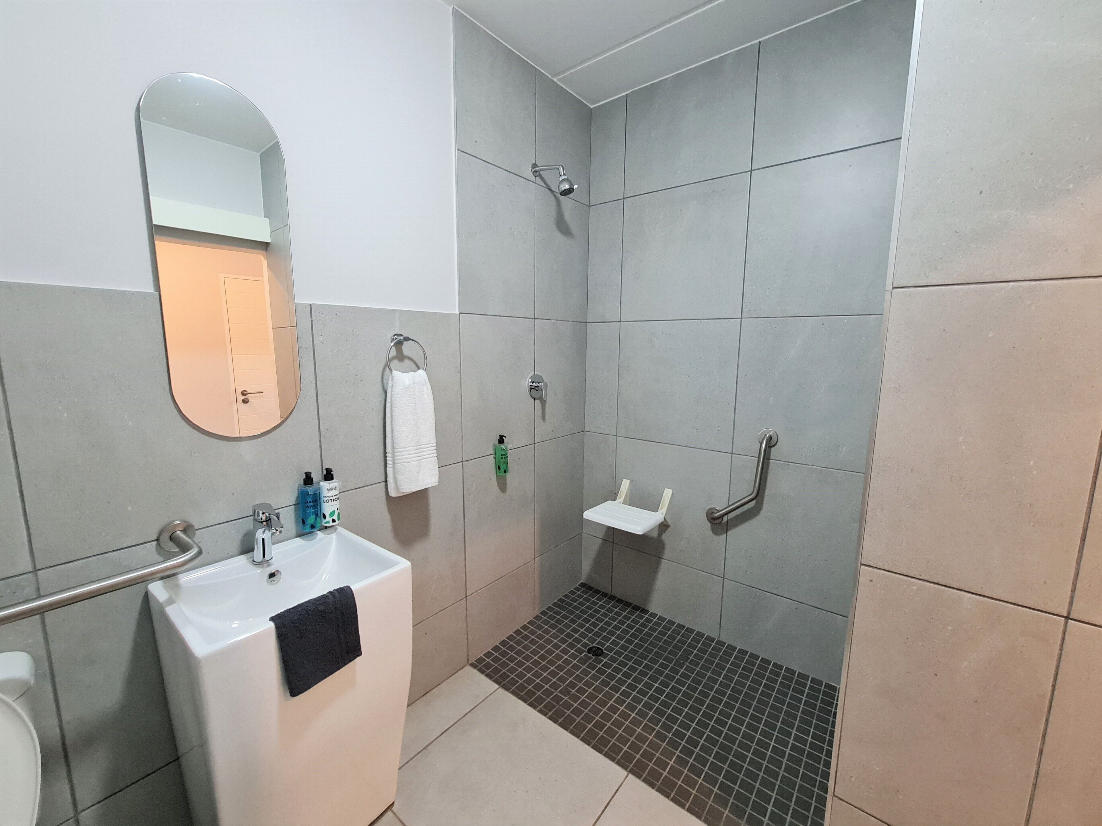 A bathroom with a sink, mirror, towel rack, shower, and grab bars.