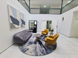 A modern living room with a grey sofa, two yellow armchairs, a coffee table, and a rug. A vending machine is visible in the background.