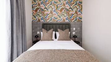 Una habitación de hotel moderna con una cama grande, un cabecero estampado y un diseño abstracto y colorido en la pared.