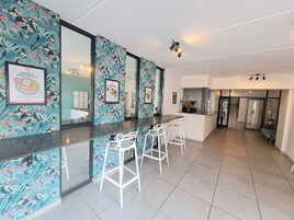 A modern kitchen with a bar area, white bar stools, and a tiled floor.