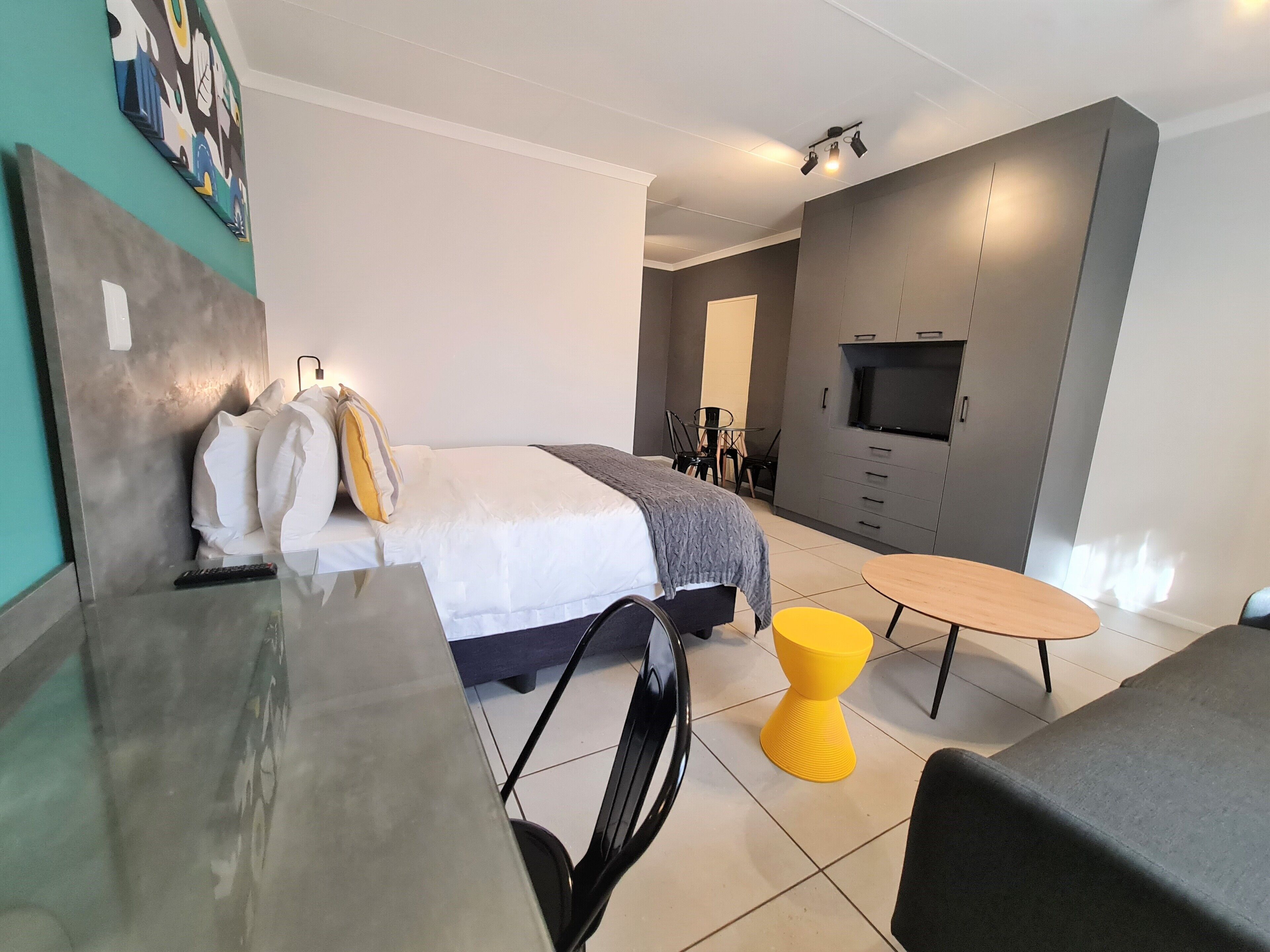 A modern hotel room with a bed, a desk, a chair, a small table, and a TV.