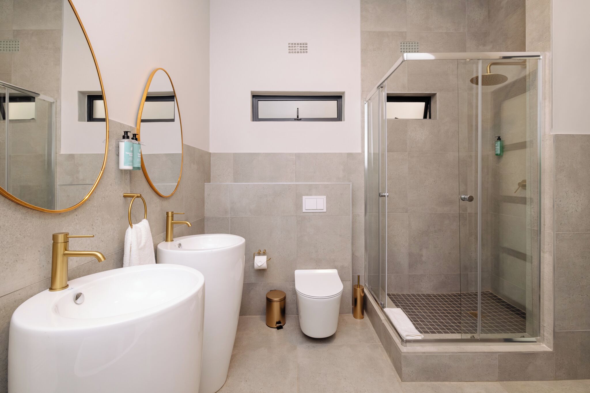 A modern bathroom with two sinks, a toilet, a shower, and a large mirror.