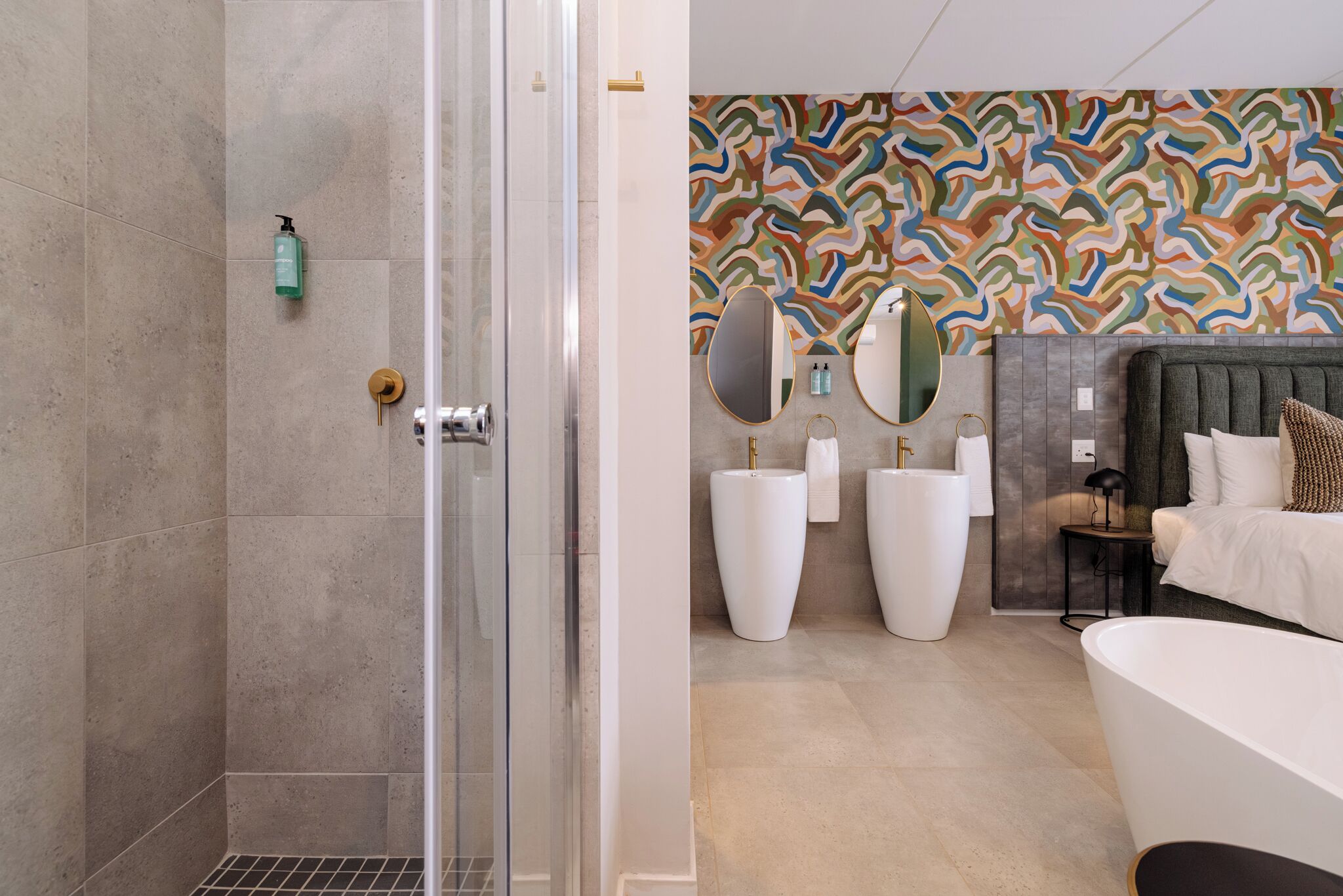 A modern bathroom with a shower, large white vases, and a bed with a headboard.