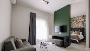 Una habitación de hotel moderna con sofá, una mesita redonda, televisor, escritorio y cama.