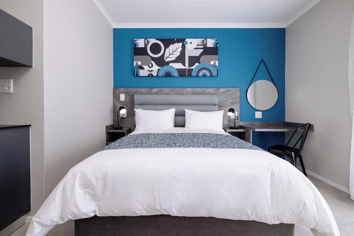 A modern bedroom with a bed, nightstands, a desk, and a wall art piece.