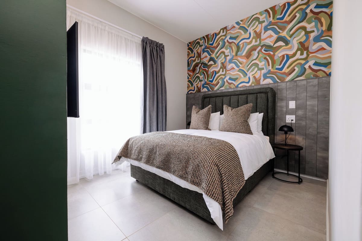 A modern bedroom with a large bed, a patterned wall, and a small bedside table.