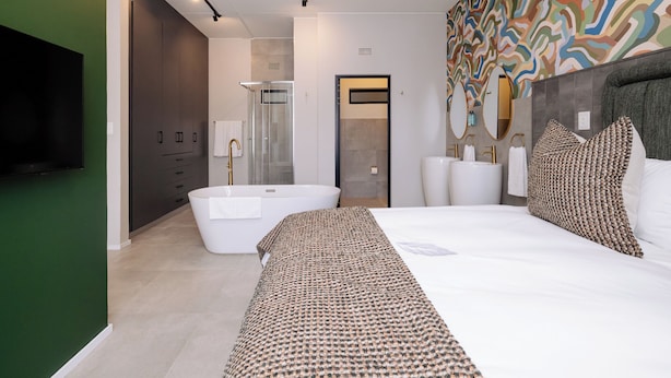 Un dormitorio moderno con una cama grande, una bañera, una ducha a ras de suelo y un televisor.