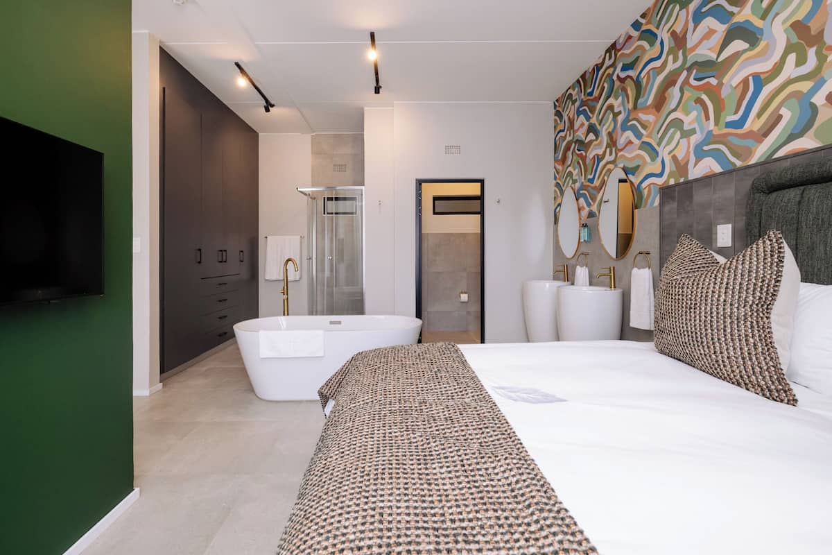 A modern bedroom with a large bed, a bathtub, a walk-in shower, and a television.
