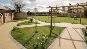 Un jardin agrémenté d’une pergola en bois, d’un bâtiment en briques et d’une pelouse verdoyante.