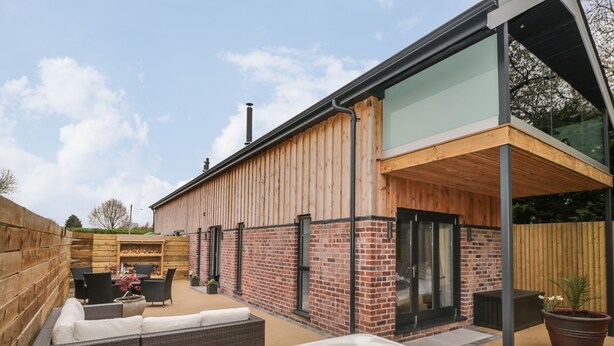 Une terrasse extérieure moderne, dotée d’un jacuzzi, de meubles en osier et d’une clôture en bois.