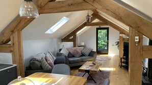 Un salon chaleureux de style industriel, avec un plafond en bois, un canapé gris, une table à manger en bois et un téléviseur.
