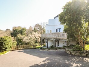 A white building with a balcony, surrounded by greenery and a gravel driveway. - Dovefields (Helston)