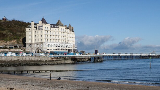 Un grand hôtel à plusieurs étages, reconnaissable à son imposante enseigne « Grand Hôtel », situé au bord de l’eau, avec une jetée qui s’avance dans l’eau.