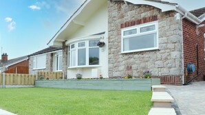 Une maison à deux étages avec une façade en pierre, une baie vitrée et une pelouse bien entretenue.