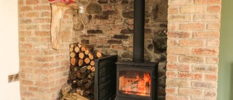 A stone fireplace with a black wood-burning stove, logs stacked beside it, and a metal shelf above.