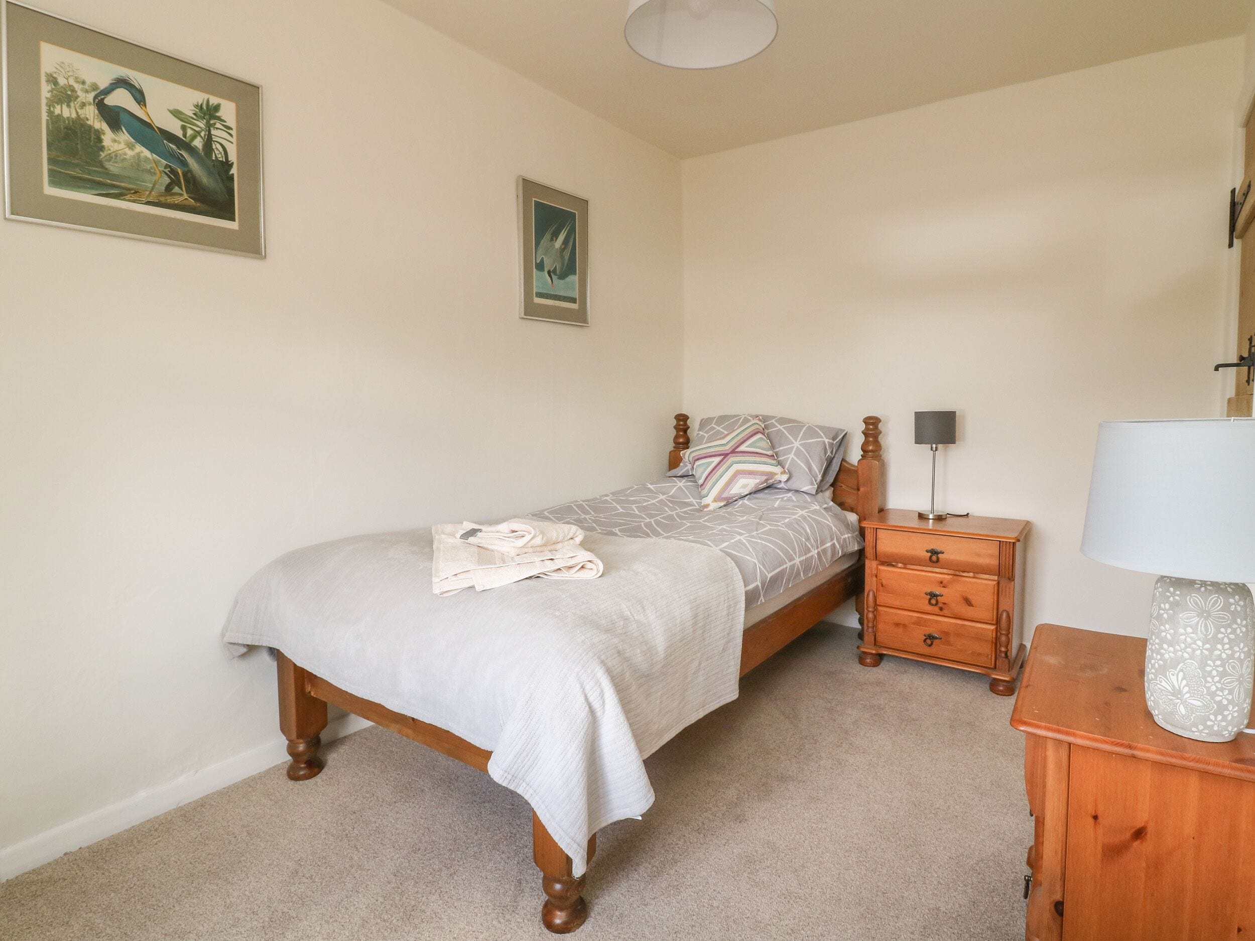 Un dormitorio con cama, mesita de noche, lámpara y dos cuadros enmarcados en la pared.