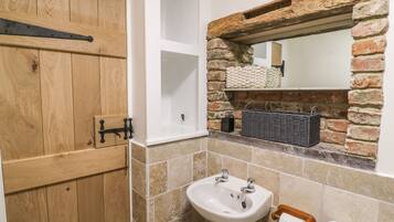 Une salle de bain avec une porte en bois, un lavabo blanc, un miroir surmonté d’une arche en briques et des toilettes.