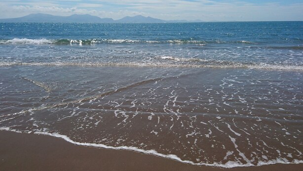 A beach with waves, a clear sky, and distant mountains. - Idan House (Llanfairpwllgwyngyll)
