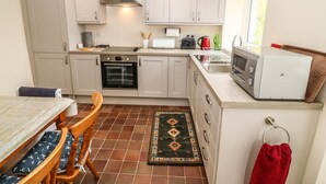 A compact kitchen with a built-in oven, microwave, and toaster. There is a dining table with chairs and a rug on the floor. - Idan House (Llanfairpwllgwyngyll)
