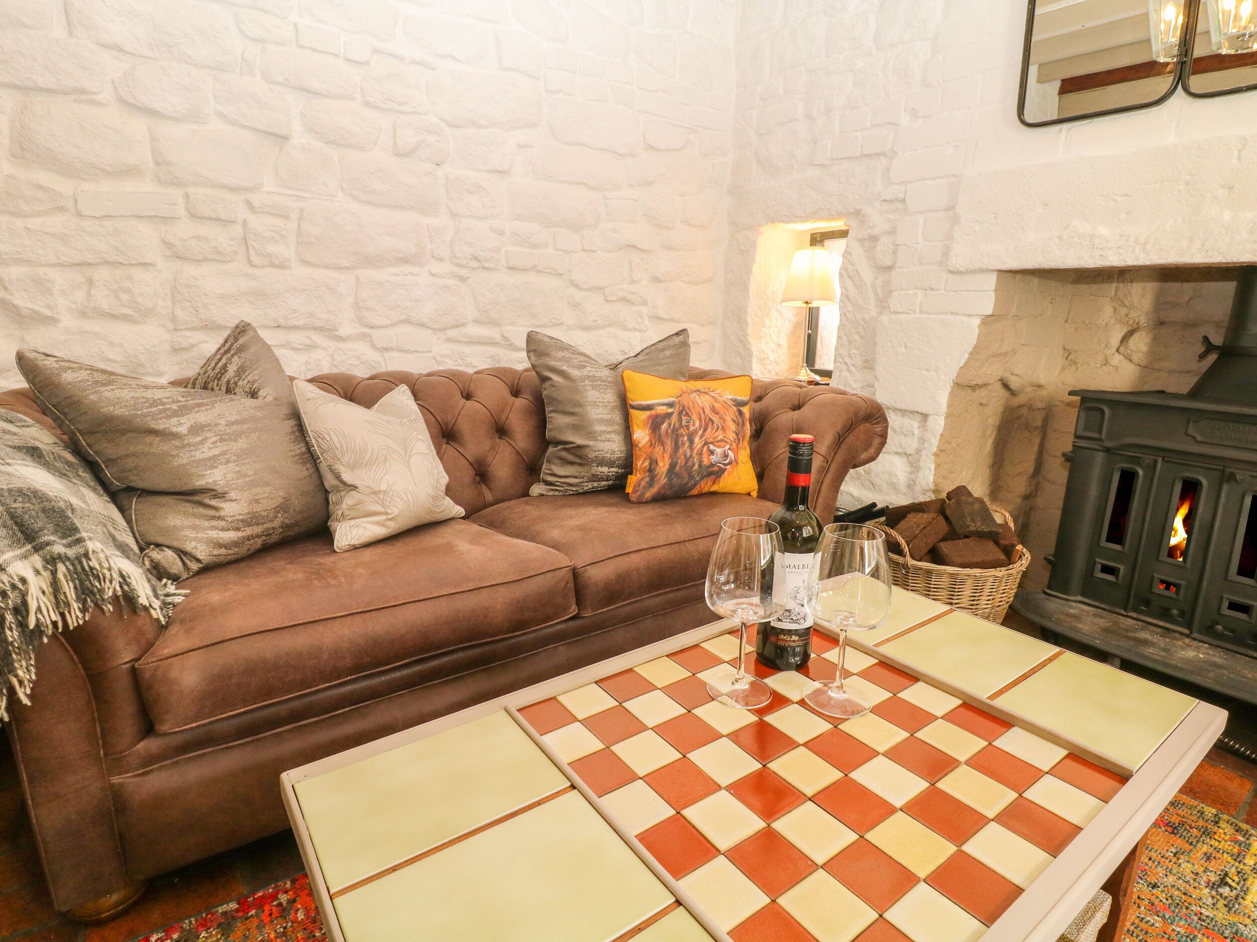 A cozy living room with a brown leather sofa, a checkered coffee table, and a stone fireplace.