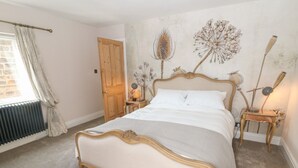 Une chambre à coucher avec un lit en bois, un radiateur, une porte et un mur orné d’œuvres d’art florales.