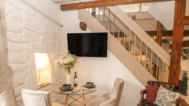 Un coin repas avec une table dressée pour deux personnes, un canapé et un escalier en arrière-plan.