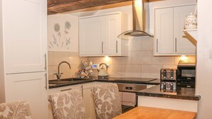 Una cocina compacta con armarios blancos, una mesa de madera y sillas estampadas.