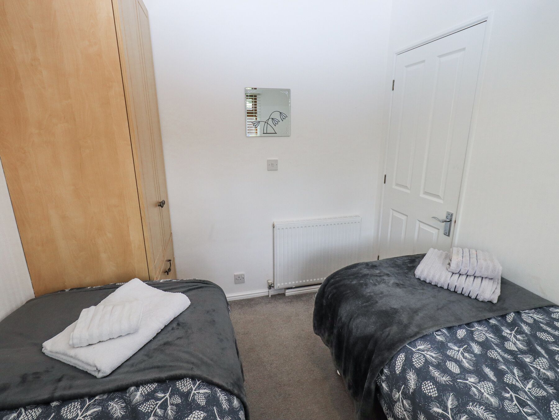 A small, clean room with two beds, a radiator, and a door.