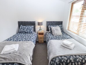 Une chambre à deux lits, chacun étant équipé d’une couette grise et d’oreillers assortis, d’une table de chevet avec une lampe et d’une fenêtre avec des stores.