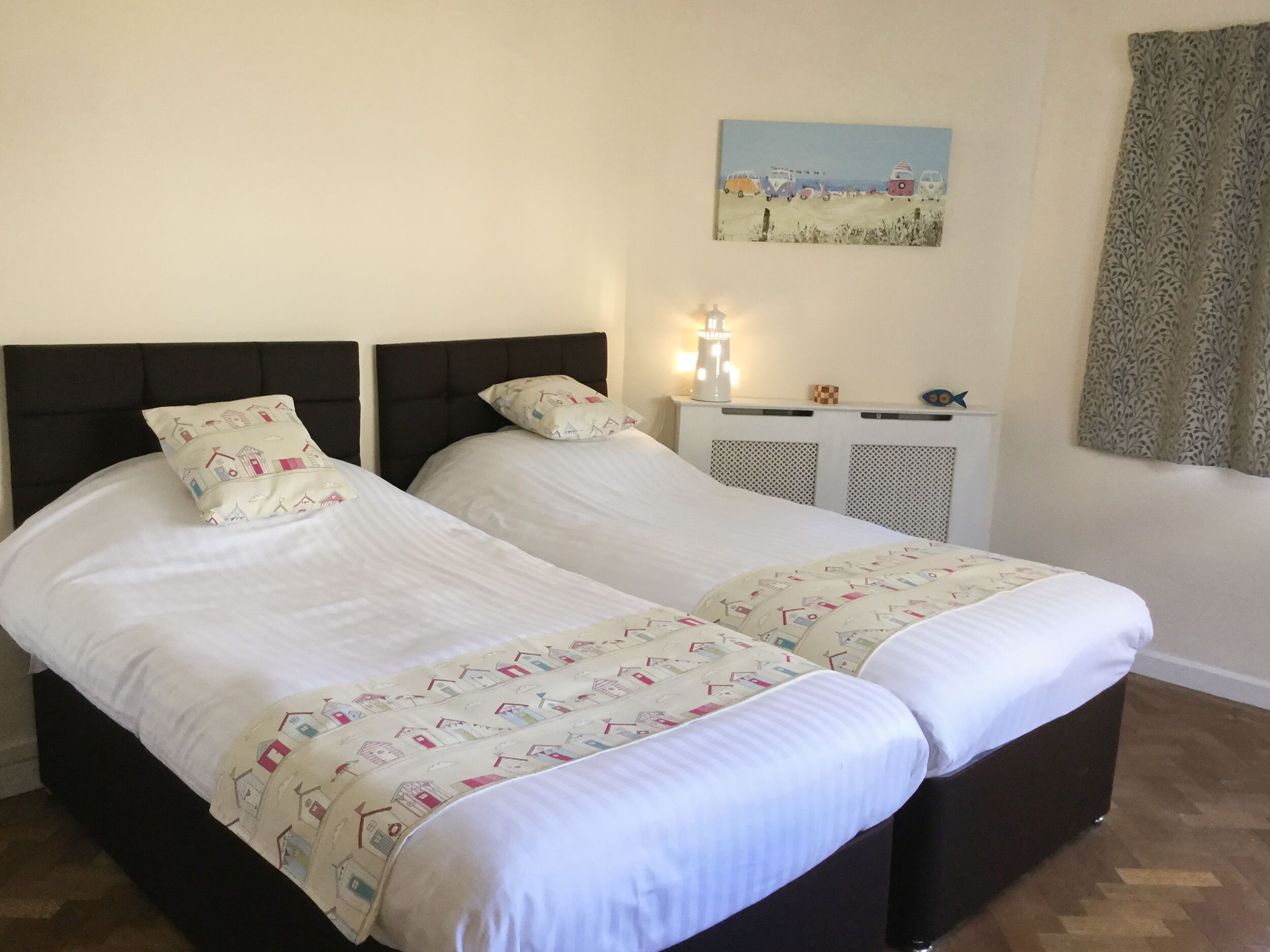 Ein Doppelbett mit weißer Bettwäsche und gemusterten Kissen, ein Nachttisch mit Lampe sowie ein Wandbild.