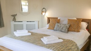 A neatly made bed with white linens, two white towels, and a woven throw blanket.