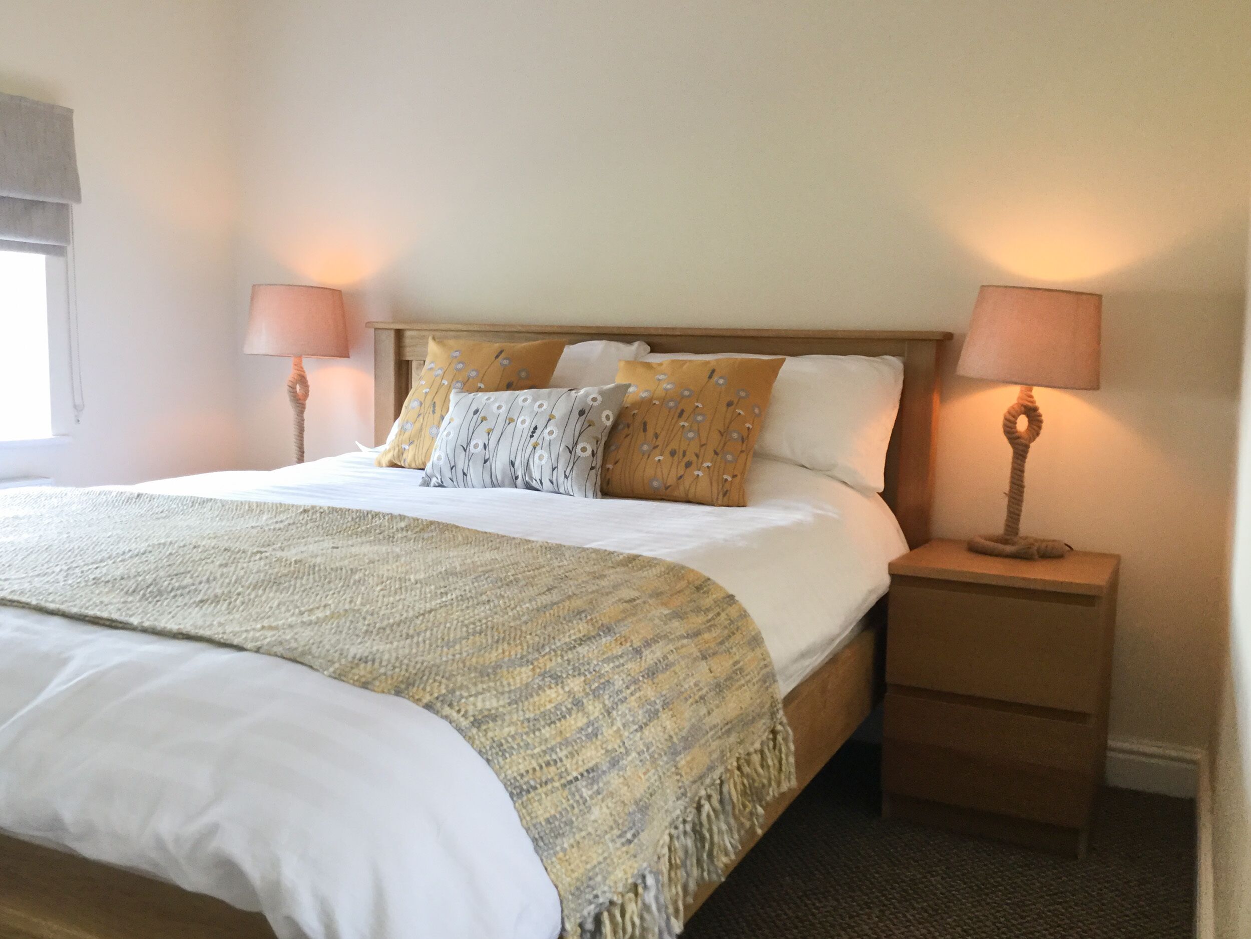 A neatly made bed with a patterned throw, two bedside lamps, and a wooden nightstand.