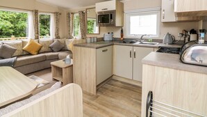 A compact living space with a kitchenette, a sofa with cushions, a small table, and a window with curtains. - Ochenta (Ilfracombe)