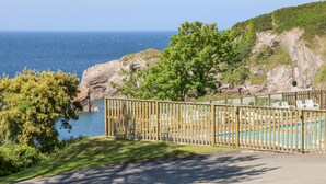 A pool area with a wooden fence, chairs, and a view of the sea and rocky cliffs. - Ochenta (Ilfracombe)