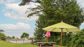 A picnic area with wooden tables and benches, a yellow umbrella, and a view of the sea. - Ochenta (Ilfracombe)